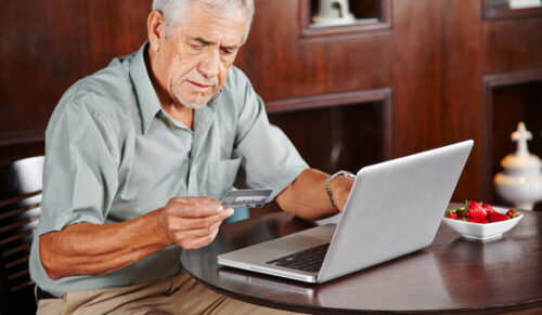 Senior am Laptop bezahlt mit seiner Kreditkarte im Internet