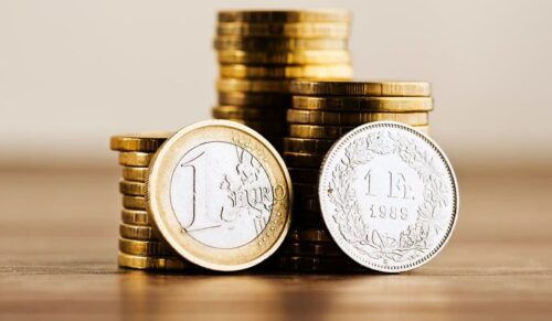 one euro coin and one swiss frank and gold money on the desk