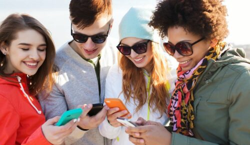 people, friendship, cloud computing and technology concept - group of smiling teenage friends with smartphone outdoors