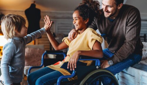 Happy multiethnic loving family. Smiling little girl with disability in wheelchair at home
