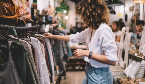 Caucaisan female customer with curly hair buying clothes in boutique using fitting concept while choosing, professional stylist creating trendy look concentrated on selection in designer shop