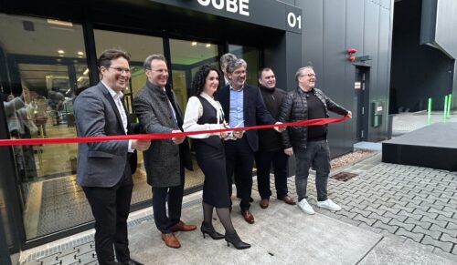 Das Rote Band des Brand Cube wird durchtrennt – und das neue Gebäude auf dem ANWR-Campus damit offiziell eröffnet: (v.l.n.r.): ANWR-Vorstand Tobias Eichmeier, Alexander Böhn, Kreisbeigeordneter des Landkreises Offenbach, die ANWR-Vorstände Martina Novotny und Frank Schuffelen, Mainhausens Bürgermeister Frank Simon und Frank Risse, Geschäftsführer der Werbegemeinschaft des O1. Im Hintergrund: der Vorsitzende des ANWR-Aufsichtsrats, Holger Baierl. (Foto: Redaktion)